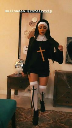 a doll dressed up in a nun outfit and holding a cross on her chest, standing next to a table