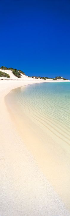 an empty beach with white sand and clear blue water