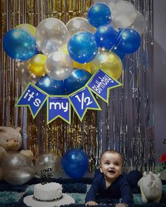 a baby sitting in front of a cake and balloons