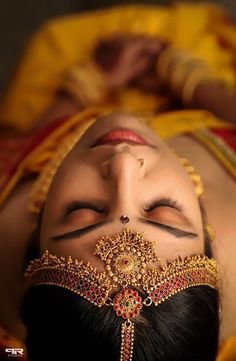 a woman with her eyes closed wearing a gold and red headdress is laying down