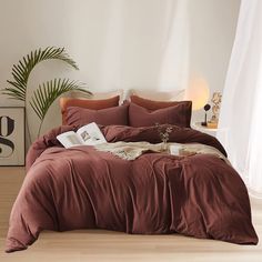 a bed with brown sheets and pillows in a room next to a plant on the floor