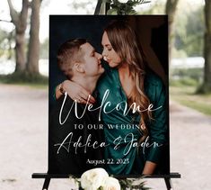 a welcome sign with a couple kissing on the cheek and flowers in front of it