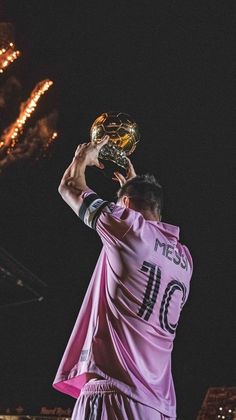 a man holding up a soccer ball in front of his face with fireworks behind him