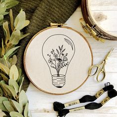 an embroidered light bulb with flowers in it next to scissors and other crafting supplies