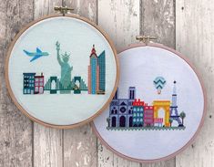 two cross - stitch hoops with cityscapes on them, one has an airplane flying over the statue of liberty