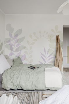 a bed sitting in a bedroom next to a wall with leaves painted on the walls