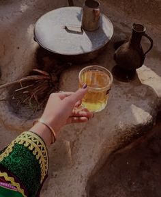 a woman holding a glass of beer in front of an open fire place with pots on the side