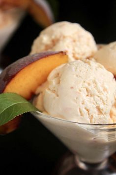 two scoops of ice cream in a glass bowl with peaches on the side