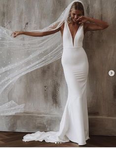 a woman in a white wedding dress with a veil over her head, leaning against a wall