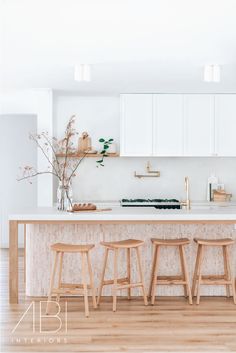 three stools sit in front of an island counter with white cabinets and wood flooring