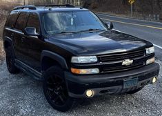 a black chevrolet suburban is parked on the side of the road in front of some trees