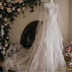 a wedding dress on display in front of a floral wall with roses and greenery