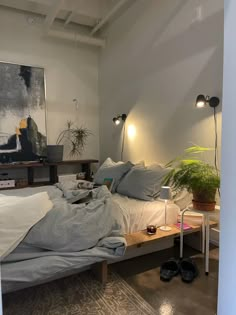 a bed sitting in a bedroom next to a table with two lamps on it and a plant