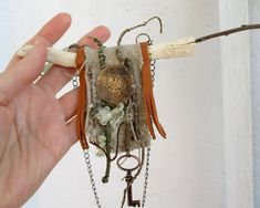 a hand holding a piece of jewelry with chains and keys attached to it, in front of a white wall