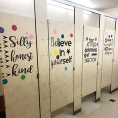 a row of restroom stalls with signs on the walls and writing on each stall door