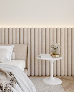 a white table sitting next to a bed on top of a wooden floor