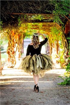 a woman in a tutu and tiara walking down a path with her hands behind her head