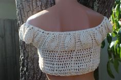 a mannequin wearing a white crochet top in front of a tree