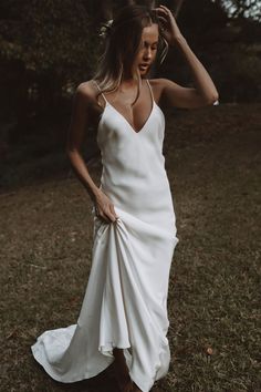 a woman in a white dress is standing on the grass with her hands behind her head