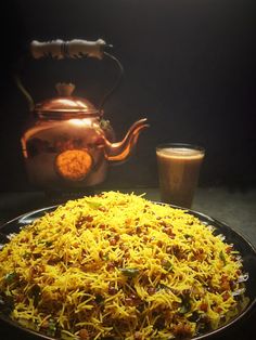 a plate full of yellow rice next to a tea pot and two cups on the table