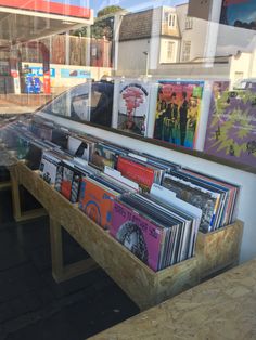 there are many records on the table in this store front window and behind it is a wooden bench that has been made out of plywood