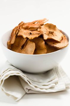 a white bowl filled with potato chips sitting on top of a table next to a napkin