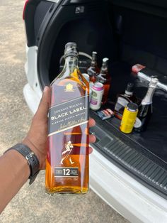 a person holding up a bottle of liquor in front of an open trunk