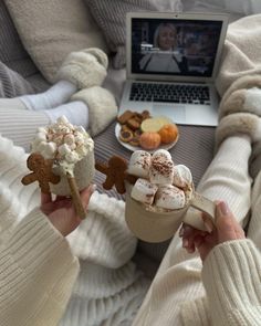 two people holding hot chocolates and marshmallows in front of a laptop