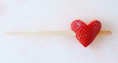 a strawberries shaped like a heart on a toothpick against a white background