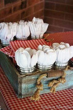 a wooden box filled with white utensils on top of a red and white checkered table cloth