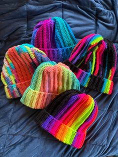 four knitted beanies laying on top of a blue bed sheet with the colors of rainbow