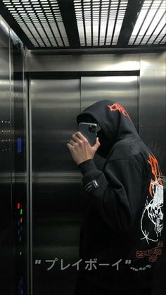 a man in a black hoodie taking a photo with his cell phone while standing in front of an elevator