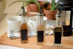 three bottles filled with different types of spices on top of a wooden tray next to cups and saucers