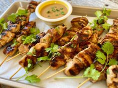 chicken skewers with cilantro, parsley and dipping sauce on a tray