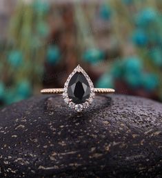 a black and white diamond ring sitting on top of a piece of rock in front of some plants