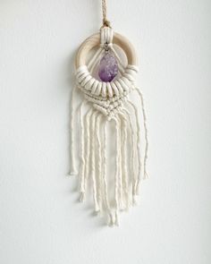 a white wall hanging with a purple stone in the center and some tassels attached to it