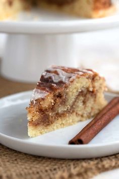 a slice of cinnamon coffee cake on a white plate with two cinnamon sticks next to it