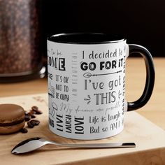 a black and white coffee mug sitting on top of a wooden table next to a spoon