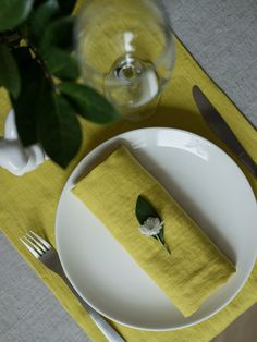 a place setting with yellow napkins and white plates, silverware and green leaves