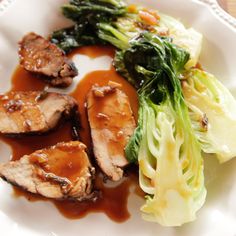 a white plate topped with meat and veggies covered in gravy on top of a wooden table