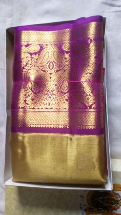 a purple and gold saree in a box on a white tablecloth with an ornate design