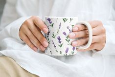 a woman is holding a coffee cup with lavender flowers on it and she has her hands wrapped around the mug