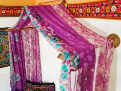 a bed covered in purple and pink fabric next to a wall hanging on a hook