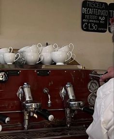 an espresso machine with many cups on it and a man standing next to it