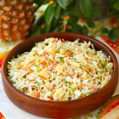 a wooden bowl filled with coleslaw on top of a table next to a pineapple