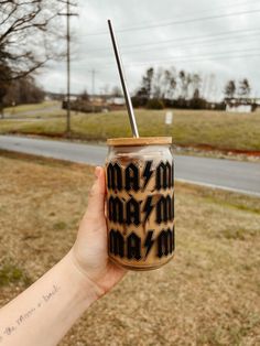 a person holding up a mason jar with a straw in it on the side of a road