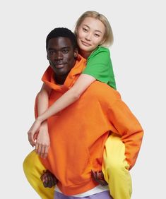 a man holding a woman on his back while she is wearing an orange and green shirt