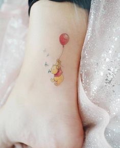 a small winnie the pooh tattoo on the right side of the foot with a red balloon