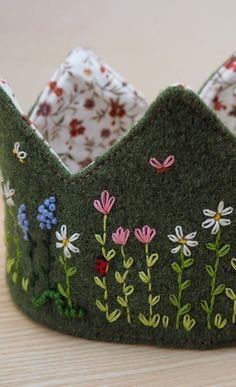 a green crown with flowers on it sitting on a wooden table next to other items