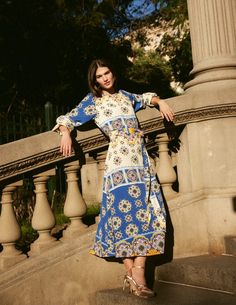 a woman is standing on some steps wearing a blue and white dress with floral print